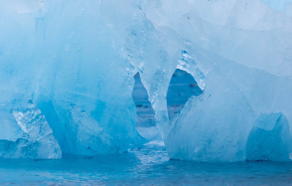 Close-up of a turquoise iceberg with an arch-shaped opening, reflecting shades of blue in the water below.