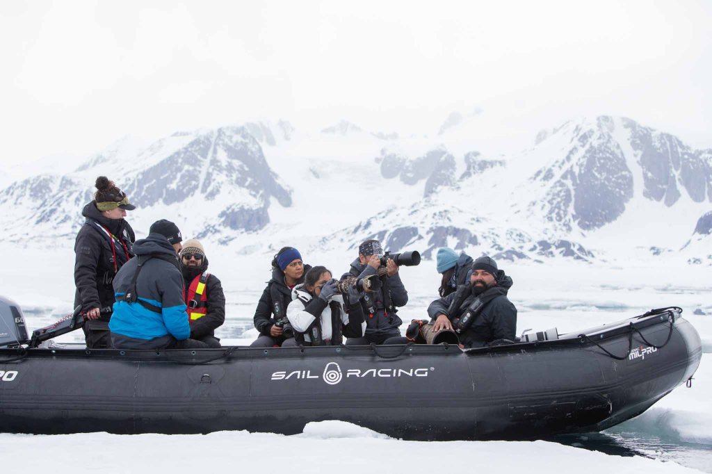 A group of people aboard a zodiac boat in the Arctic, surrounded by snowy mountains and icy waters, preparing for wildlife observation and photography.